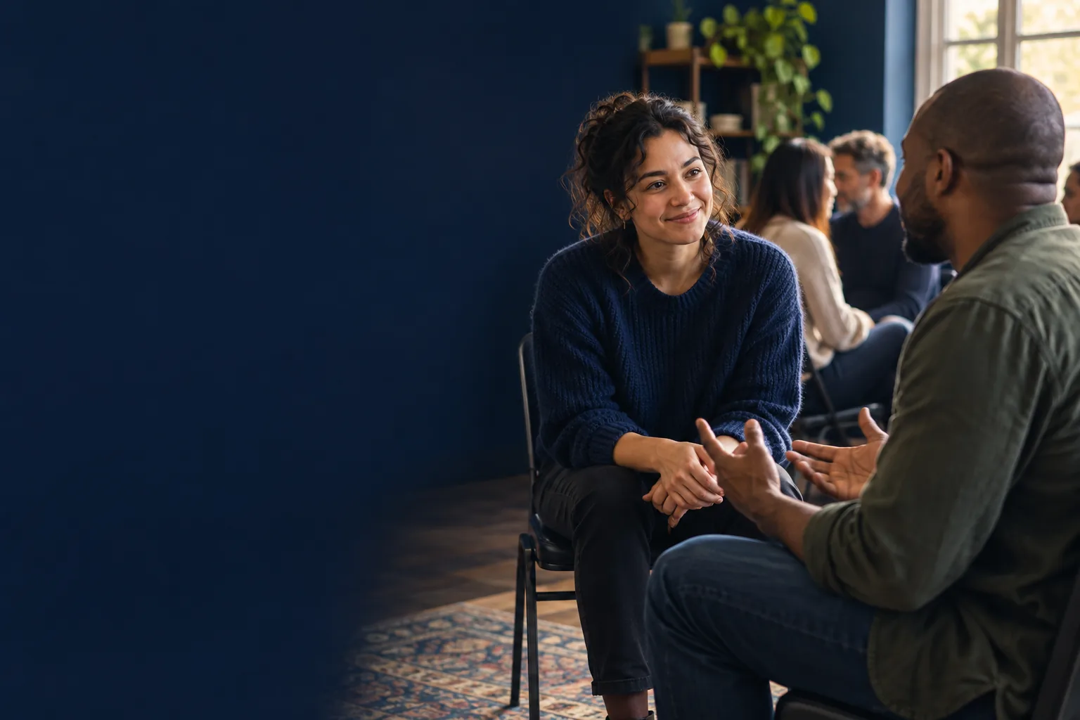 Two adults getting acquainted at a community workshop, with one listening as the other speaks.